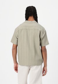Short-sleeve shirt in light olive green, featuring vertical stripes, a collar, and a relaxed fit. Made from soft, textured fabric.