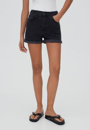 Shorts en denim noir avec un ourlet retroussé, une taille élastique et des poches avant, associés à des tongs noires plates.
