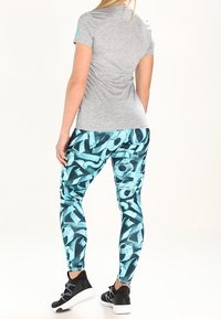 Camiseta deportiva gris combinada con leggings de patrón abstracto en color azul verdoso. Los leggings tienen una textura suave y son ajustados. Zapatillas negras completan el atuendo.