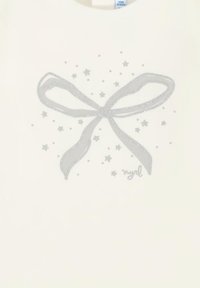 T-shirt bianco in tessuto con un design di fiocco argentato scintillante e piccole stelle sparse attorno. Collo semplice e arrotondato e maniche corte.