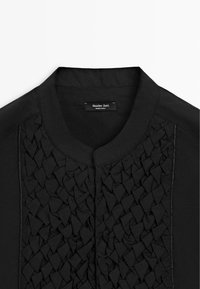 Černá košile s kulatým límečkem a texturovaným, geometrickým skládacím vzorem na předním panelu, označená Massimo Dutti.