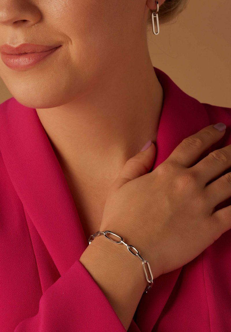Silver chain bracelet with oval links, worn on a hand. Accompanied by pink fabric, showcasing a smooth texture and clean design.