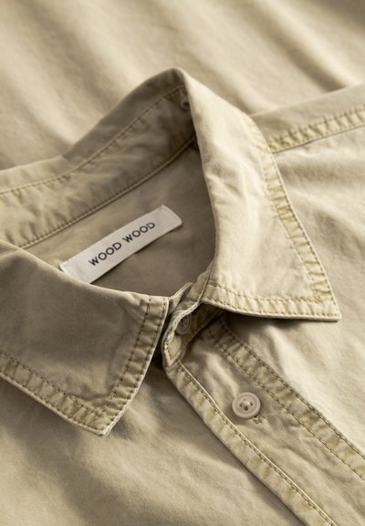 Beige button-up shirt with a collared neck, featuring a soft, textured fabric, and a label reading "WOOD WOOD" on the inside collar.