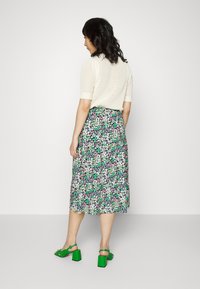 Saia midi floral com padrões em verde, rosa e branco; combinada com um top de malha canelada em creme; sandálias de salto bloco verde.