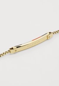 Gullfarget armbånd med en jevn metallisk overflate, flerfargede stripete detaljer og en lås med "HILFIGER" gravert.