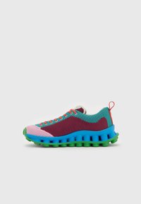 Shoe atlética colorida com um cabedal em malha texturizada nas cores roxa, rosa e teal, apresentando uma sola grossa azul e verde com acentos laranja.