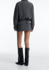 Grå langærmet trøje med en afslappet pasform, parret med en matchende kort nederdel med baglommer og knæhøje sorte støvler.