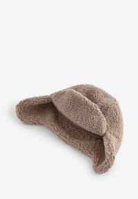 Bonnet en polaire brun clair avec des rabats pour les oreilles et une texture douce. Le design est arrondi, avec une bande cousue le long de la base.