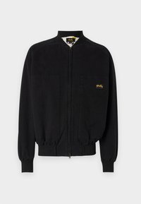 Black zip-up jacket made of smooth fabric, featuring a band collar, two front pockets, ribbed cuffs, and a small logo on the left chest.