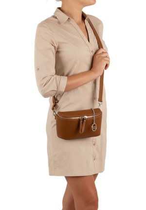 Brown leather crossbody bag with a zippered compartment, textured surface, slim shape, and silver hardware accents, worn at the hip.