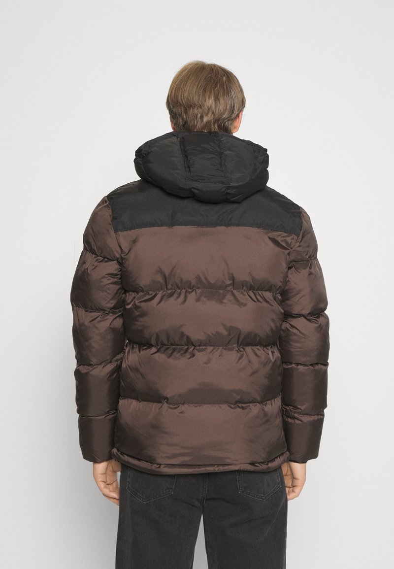 Veste rembourrée marron et noire avec une capuche, présentant une texture brillante et des sections cousues. Les manches et le corps ont un design matelassé.