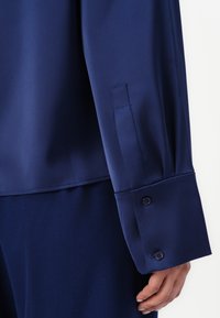 Camicia a maniche lunghe blu navy con tessuto morbido, polsini con bottone e vestibilità sartoriale con una leggera lucentezza.