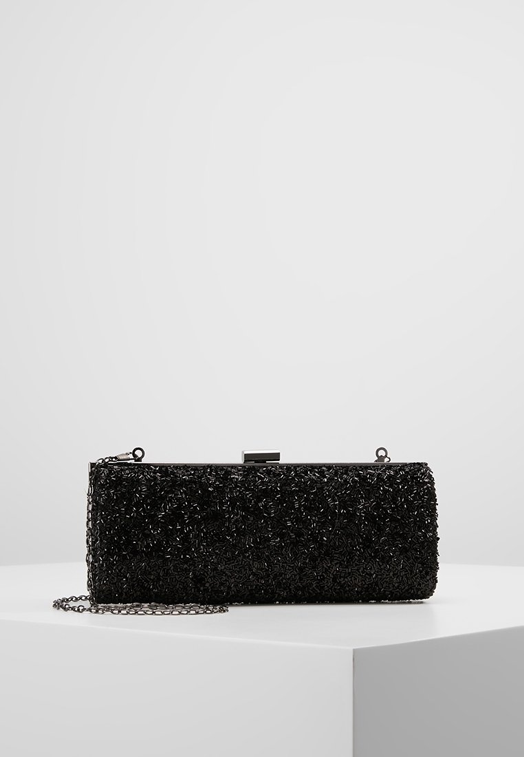 Pochette noire en matière texturée avec perles décoratives. Elle est dotée d'un fermoir argenté et d'une bandoulière chaîne amovible. Forme rectangulaire.