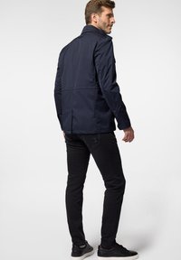 Granatowa kurtka z kołnierzem, o smukłym fasonie i gładkiej fakturze. Połączona z czarnymi dżinsami i fakturowanymi butami, widok z tyłu.