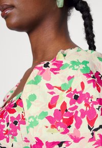 Blusa com padrão floral em tecido leve, apresentando flores em tons de rosa, verde e preto. Inclui decote redondo e detalhe de ombro franzido.