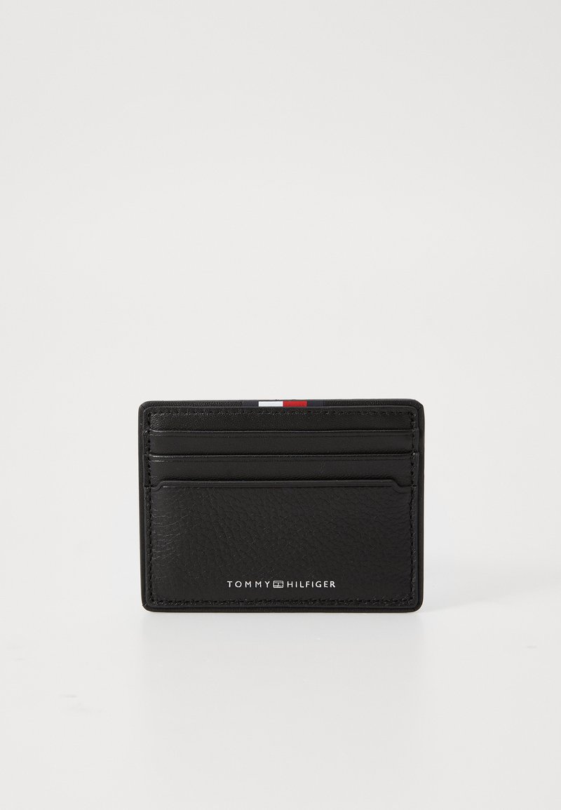 Svart lær lommebok med teksturert overflate, seks kortlommer, og en liten hvit, rød og blå aksentstripe øverst. Merking vist under.