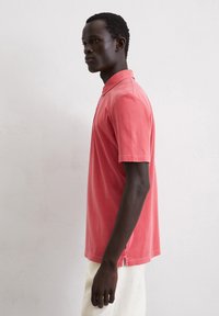 Koraalrood poloshirt van katoen met een klassieke kraag, korte mouwen en zijsplitsen aan de zoom. Eenvoudig en ontspannen pasvorm ontwerp.