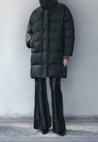 Piumino nero con design trapuntato, colletto alto e chiusura frontale. Abbinato a pantaloni in pelle nera a zampa di elefante e tacchi appuntiti neri.