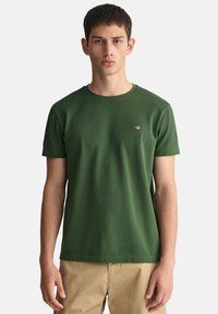 T-shirt in cotone verde con scollo rotondo e maniche corte. Presenta un piccolo logo ricamato sul petto. Texture liscia.