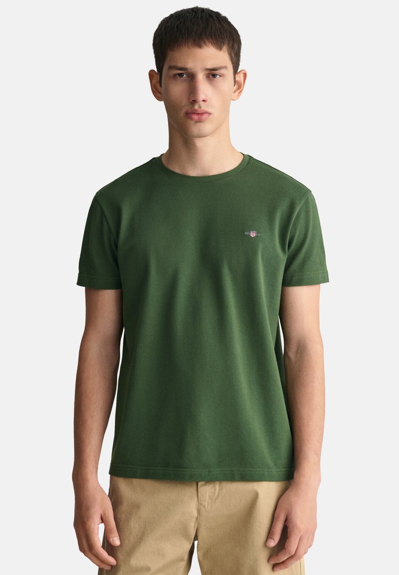 T-shirt in cotone verde con scollo rotondo e maniche corte. Presenta un piccolo logo ricamato sul petto. Texture liscia.