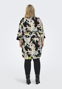 Αφέλεια, φόρεμα μέχρι το γόνατο σε πολύχρωμο αφηρημένο σχέδιο με πράσινα, ροζ και μαύρα. Διαθέτει μανίκια τριών τετάρτων και σφιχτό στη μέση.