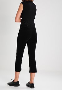 Pantalons cropped noirs en tissu doux avec une texture lisse, arborant une coupe ajustée et un ourlet qui se termine juste au-dessus de la cheville.