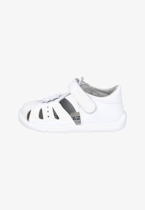 Sandalia blanca para niño pequeño con talón cerrado, puntera abierta, laterales recortados, correa de velcro y flor decorativa en la parte superior, vista lateral.