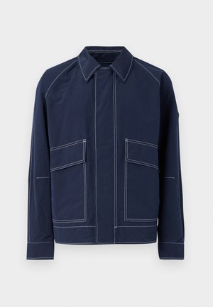 Navy blue jacket featuring a collared neck, two large front pockets, contrast white stitching, and a relaxed fit. Made from lightweight material.