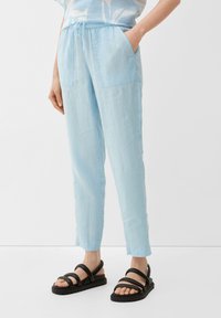 Lichtblauwe linnenbroek met een elastische tailleband, voorzien van twee voorkruiken en taps toelopende pijpen, gecombineerd met zwarte sandalen met bandjes.