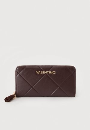 Portefeuille zippé en cuir matelassé marron foncé avec logo Valentino doré et tirette pompon sur fond uni clair.