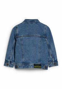 Jeansjacka i medelblått med klassisk passform, långa ärmar och en etikett längst ner med texten "DIVSN." Slitna detaljer på tyget.