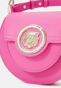 Borsa a mano in pelle rosa con dettaglio metallico a forma di testa di leone dorata circolare, design con pattina curva e superficie testurizzata. Tracolla regolabile con borchie.