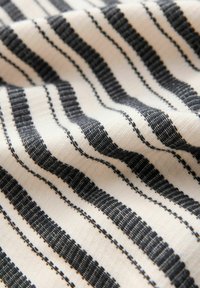 Tela de algodón con rayas alternas en negro y blanco, que presenta un tejido texturizado. El patrón incluye tanto rayas anchas como estrechas.