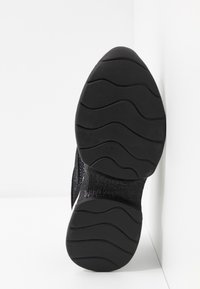 Semelle d'une chaussure noire avec des motifs ondulés et le logo "Karl Lagerfeld" embossé au centre.
