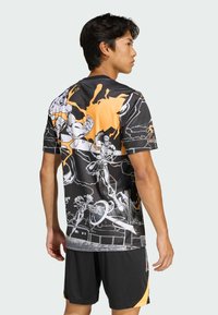Czarna i pomarańczowa koszulka sportowa z krótkim rękawem z grafikami postaci w stylu komiksowym, zestawiona z czarnymi szortami. Gładki, syntetyczny materiał.