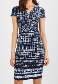 Sukienka do kolan w kolorze granatowym i białym, z fasonem kopertowym, krótkimi rękawami oraz geometrycznym wzorem o różnej grubości linii.