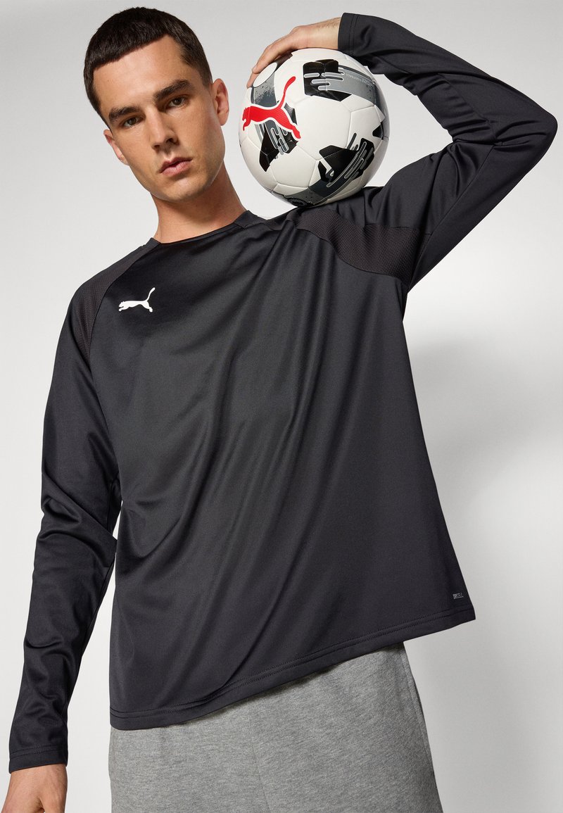 Zwarte sportshirt met lange mouwen en een gestructureerd patroon, voorzien van een wit Puma-logo, gecombineerd met grijze joggingbroek en een zwart-witte voetbal.