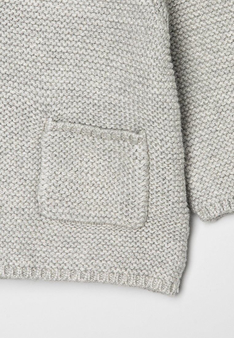 Cárdigan gris de punto que presenta un bolsillo cuadrado, puños acanalados y dobladillo. La textura es suave con un sutil patrón de punto grueso.