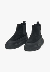 Black ankle boots featuring a combination of suede and rubber materials, a thick platform sole, elastic side panels, and pull tabs.