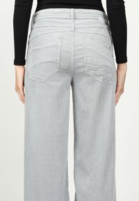 Helle graue Cordhosen mit weitem Bein, hinteren Taschen und einer strukturierten Oberfläche. Mit kontrastierenden Nähten und einem Standardbund.