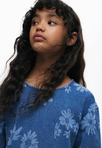 Denimblå top med blomsterprint i lysere blå nuancer, rund halsudskæring og blødt, tekstureret stof.