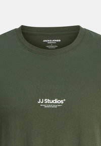 Oliven grøn bomulds t-shirt med rund hals, der har hvid tekst "JJ Studios" og yderligere brandingdetaljer nederst til venstre.