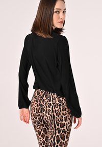 Maglietta nera a maniche lunghe abbinata a leggings aderenti con sfondo beige e motivo a leopardo scuro. Texture liscia, design casual.