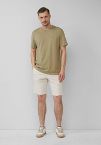 Oliwkowa koszulka z krótkim rękawem z subtelnym logo, zestawiona z kremowymi szortami. Na białych sneakersach z beżowymi akcentami kończy się stylizacja.