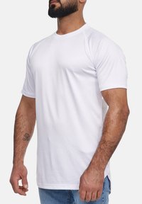 Camiseta blanca de manga corta con cuello redondo, textura suave, tela ligera y aberturas laterales para facilitar el movimiento.