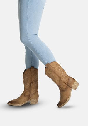 Jean skinny bleu clair associé à des bottes de cowboy en cuir marron clair mi-mollet avec des coutures décoratives et des talons carrés.