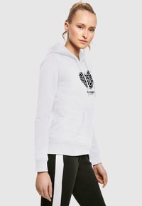 White hoodie with a leopard print heart graphic at the center, featuring a kangaroo pocket and ribbed cuffs, paired with black trousers.