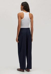 Weißes ärmelloses Tanktop kombiniert mit navy-blauen weiten Hosen. Die Hosen haben ein maßgeschneidertes Design, mit Gesäßtaschen und einer glatten Textur.