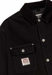 Giacca nera con colletto in corduroy, bottoni a pressione argentati e tasca sul petto con una patch del logo a fiamma "GRMY" rossa e bianca.