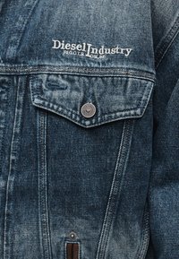 Τσέπη τζιν μπουφάν με ασημένιο κουμπί και κεντημένο λευκό λογότυπο «Diesel Industry» πάνω από το πτερύγιο της τσέπης.
